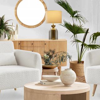 Modern minimalist living room with white armchairs, a round mirror, and plants.